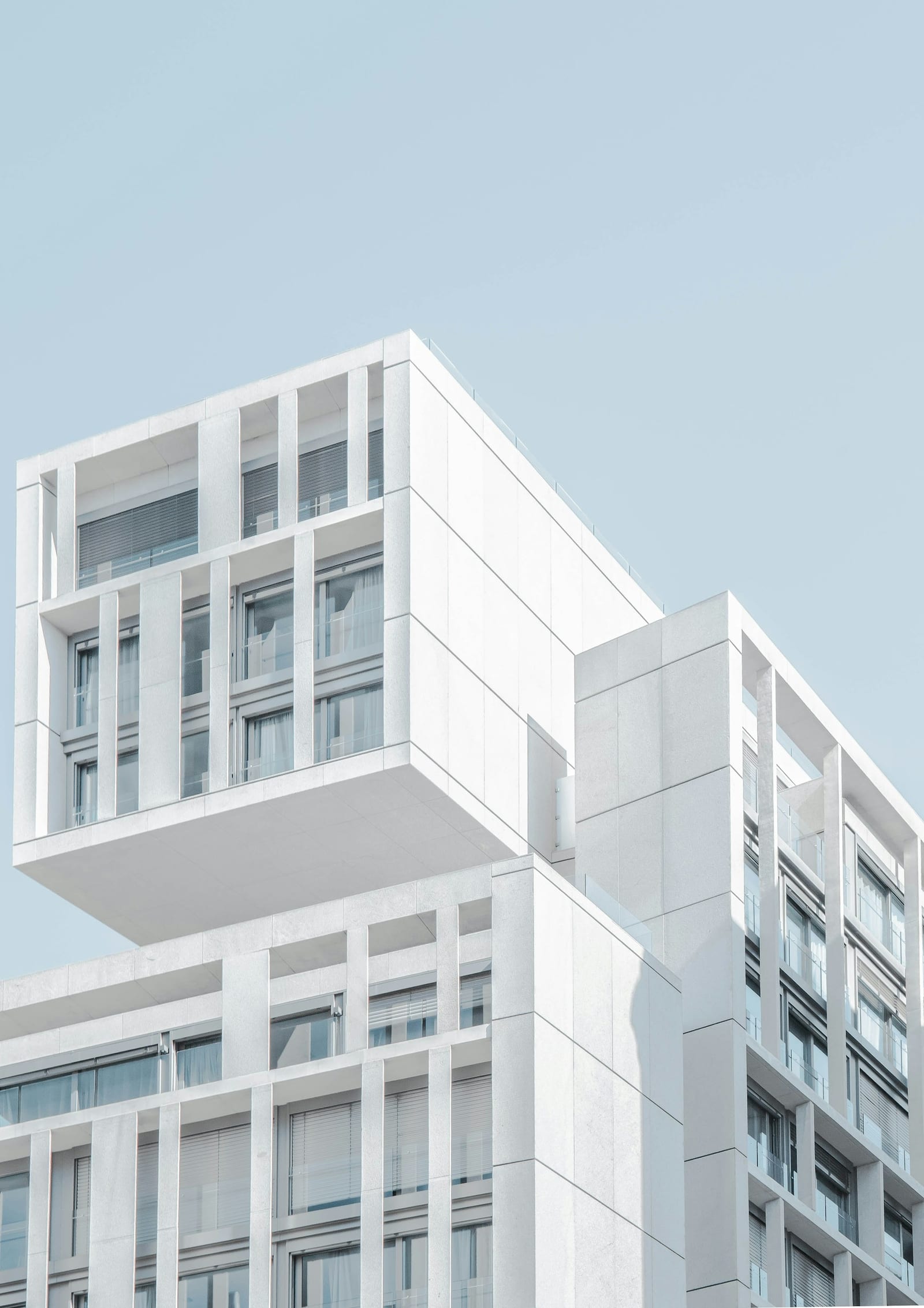 Minimalist white concrete building with abstract geometric facade under a clear sky.